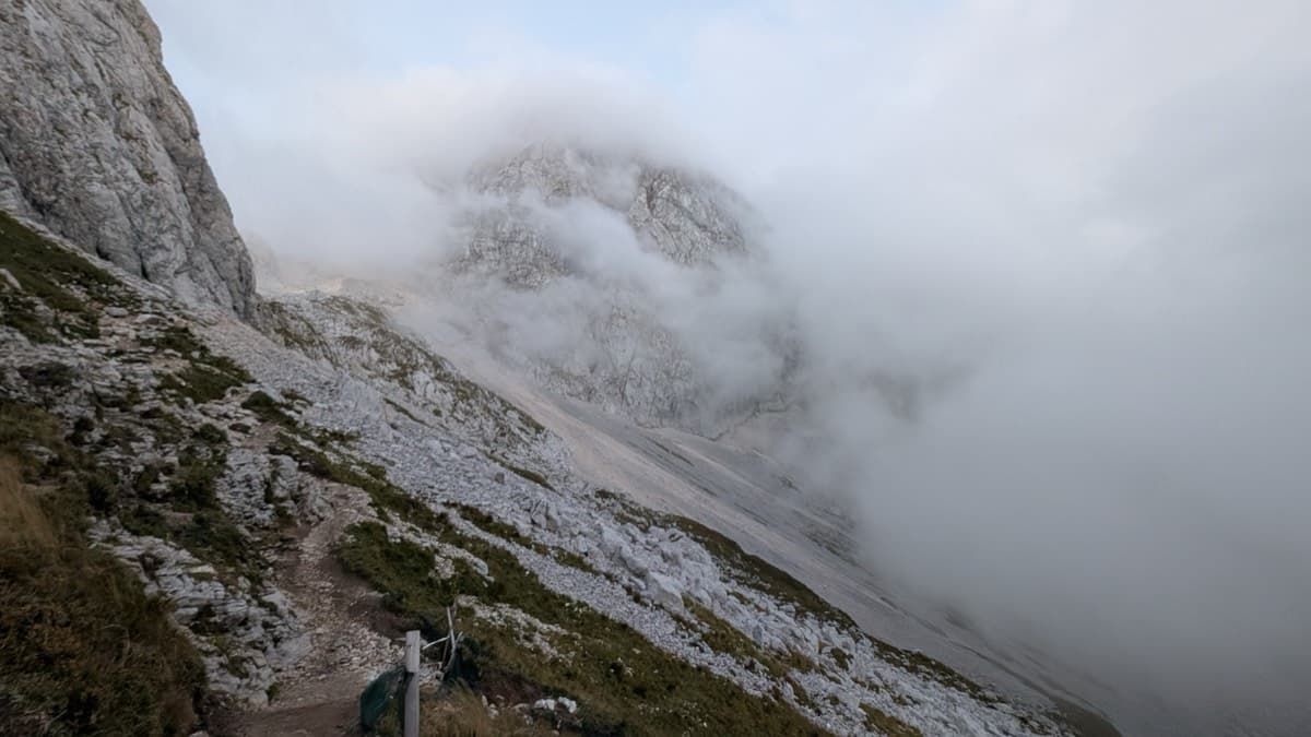The point on the marked trail above the Mangart saddle where the September 2025 party left it and began the scramble traverse to the foot of the wall (here in cloud). They found it manageable but possibly not the shortest way.