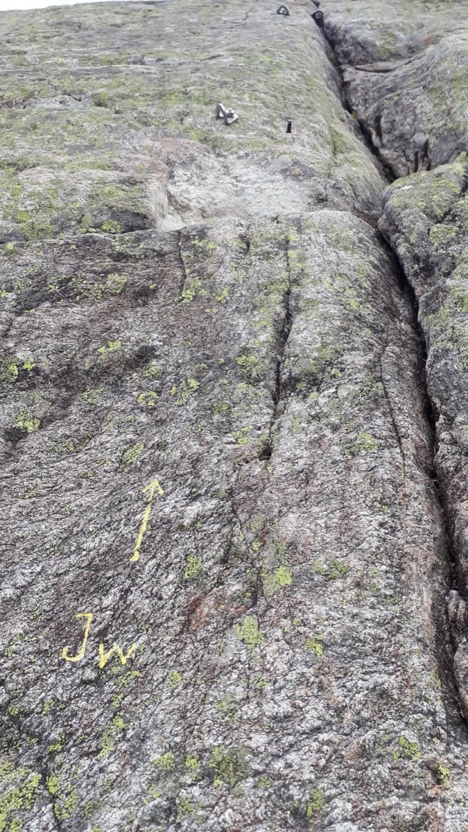 The start: 'JW' and an arrow painted in yellow on the slab, left of a deep crack.