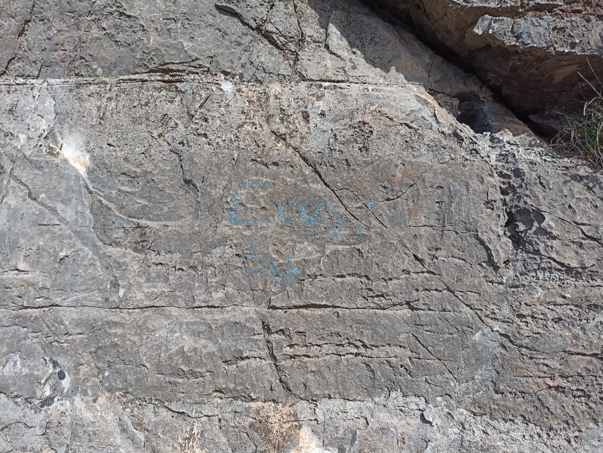 The start of Kapi Reborn as a March 2024 party found it: only a faint scrawl of blue paint on the grey rock.