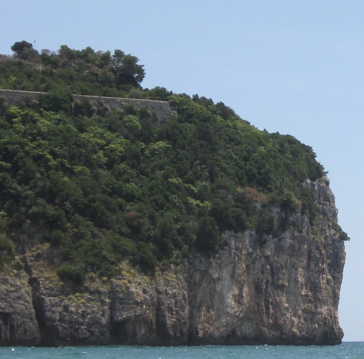 Montagna Spaccata seen from the beach at Gaeta: the wooded top of Monte Orlando and the sea cliff below it. The routes are reached by abseil from the top.