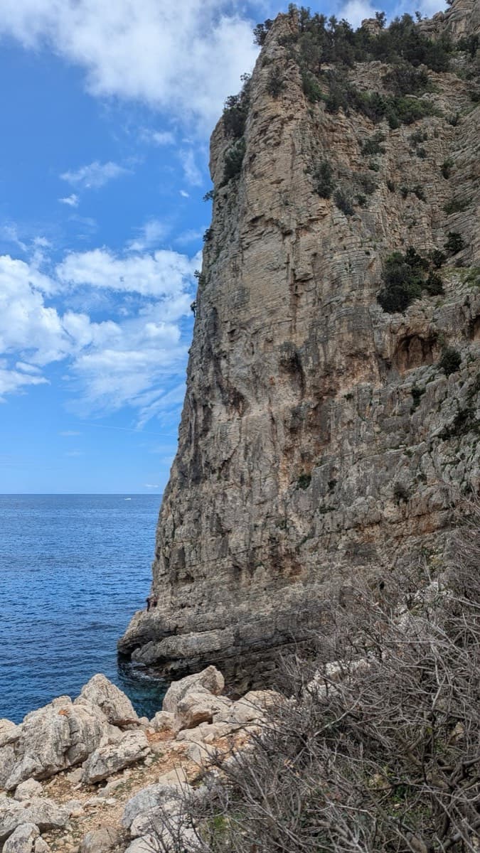 The start seen from the bottom of the steps: follow the rock ledge along the foot of the cliff to the platform at the corner, just above the water.