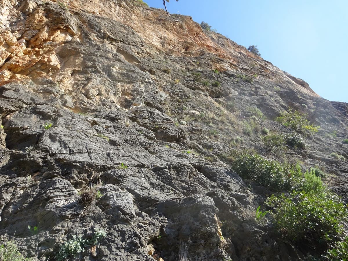 Looking up from the start of Mira (March 2022): grey, easy-angled rock at the base under orange walls.
