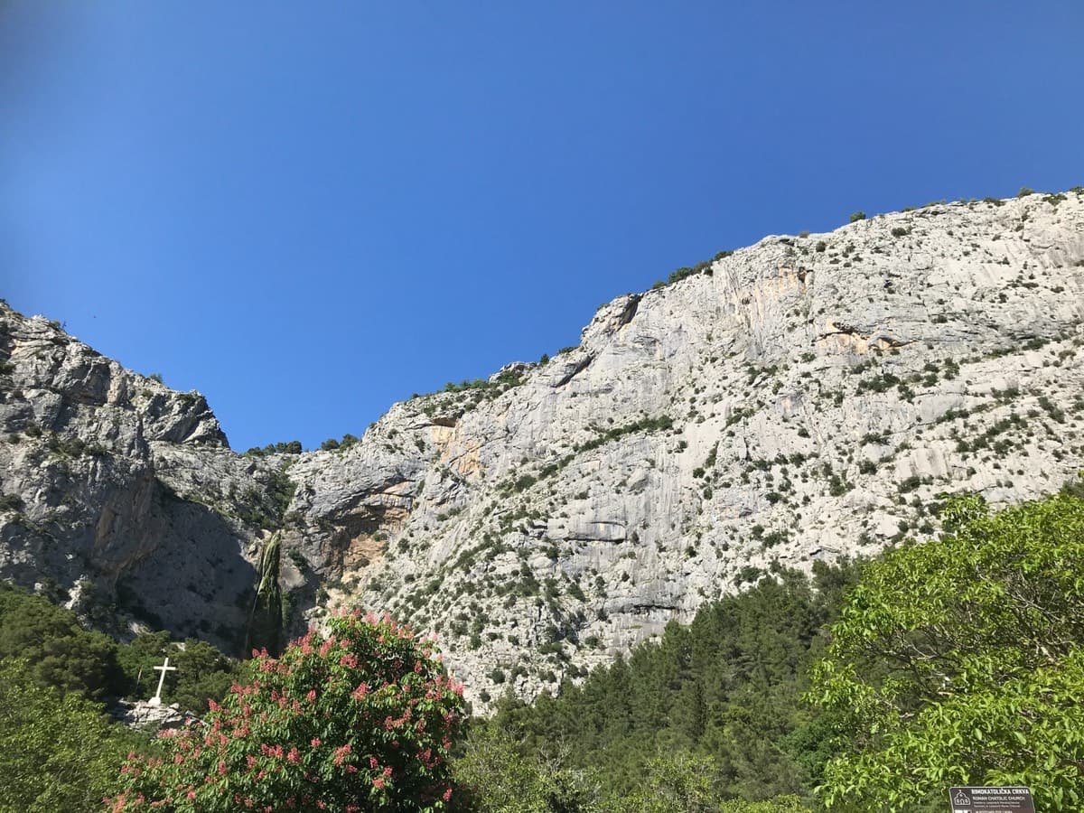The Ilinac wall seen from below (photographer's title: "the Ilinac wall"), May 2024. A white cross stands among the trees at the lower left.