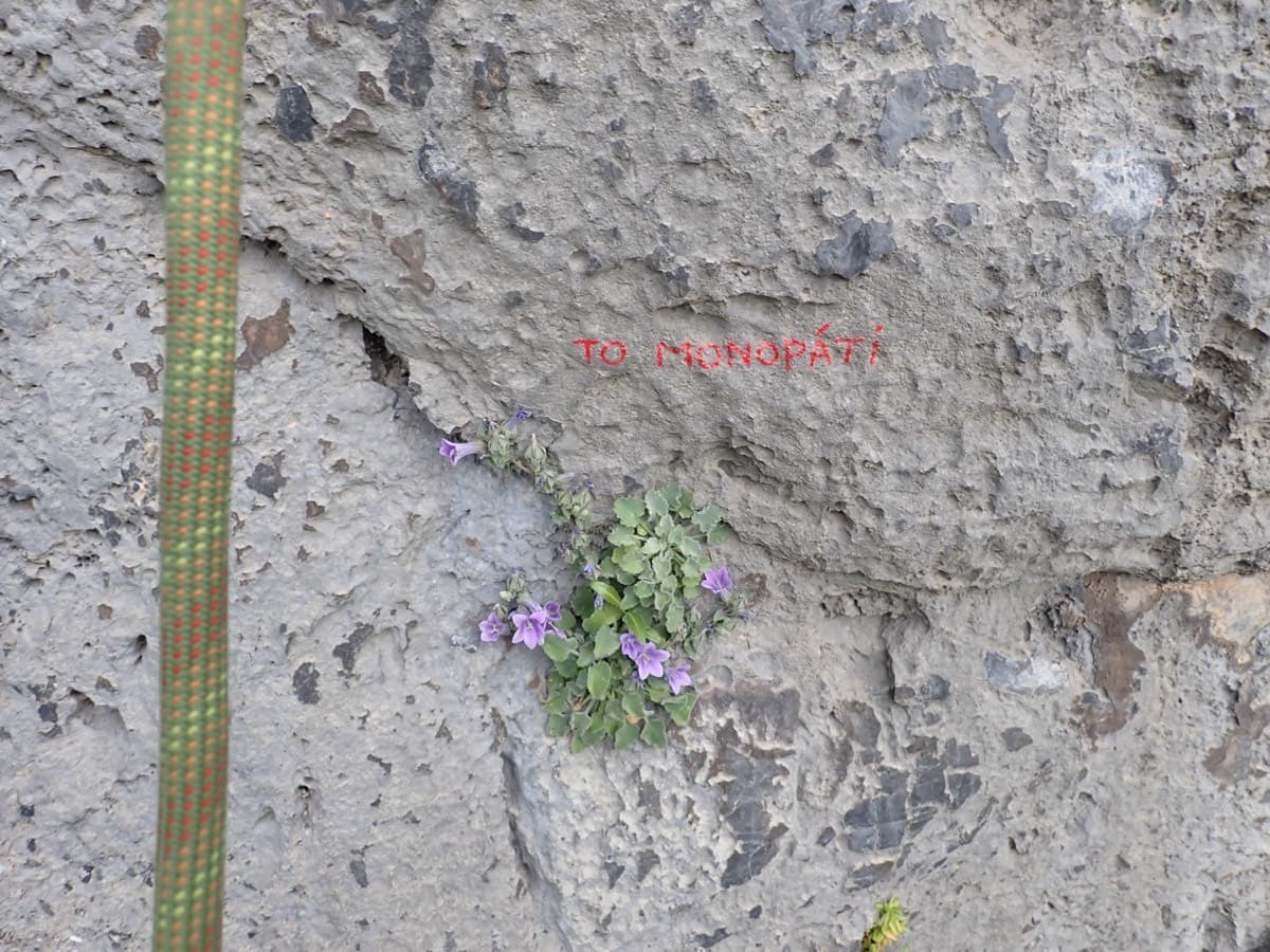 'To monopáti' painted in small red letters on the grey rock at the foot of the route (May 2026).