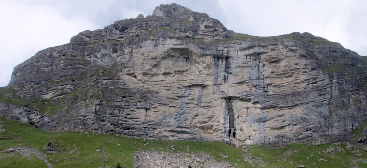 The Hintisberg wall seen from the meadows below; the marked path from the Alp climbs to the foot of the cliff.