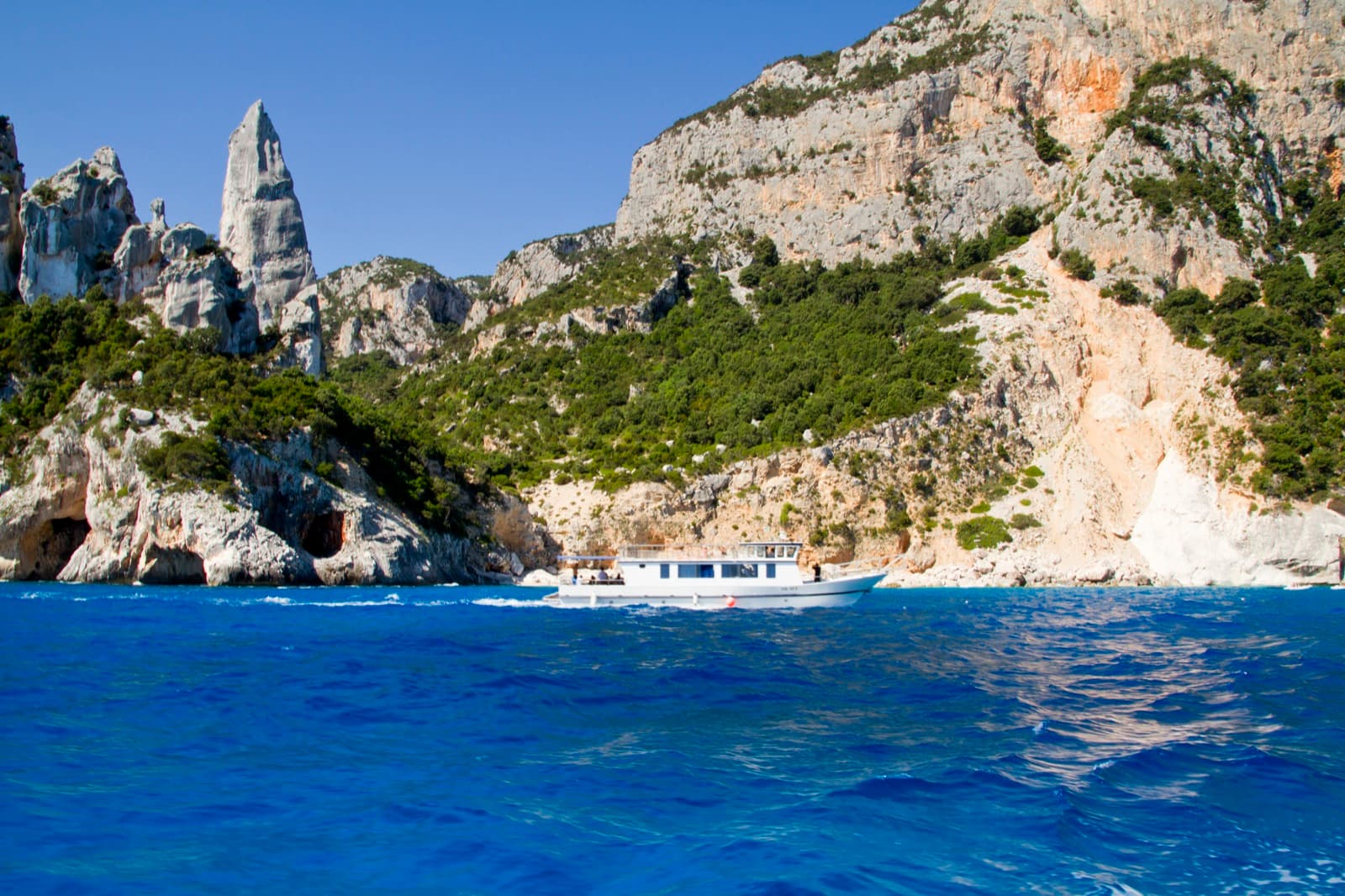 Cala Goloritzè from the sea: the Aguglia stands at the left above the sea caves, with the white beach at the right.
