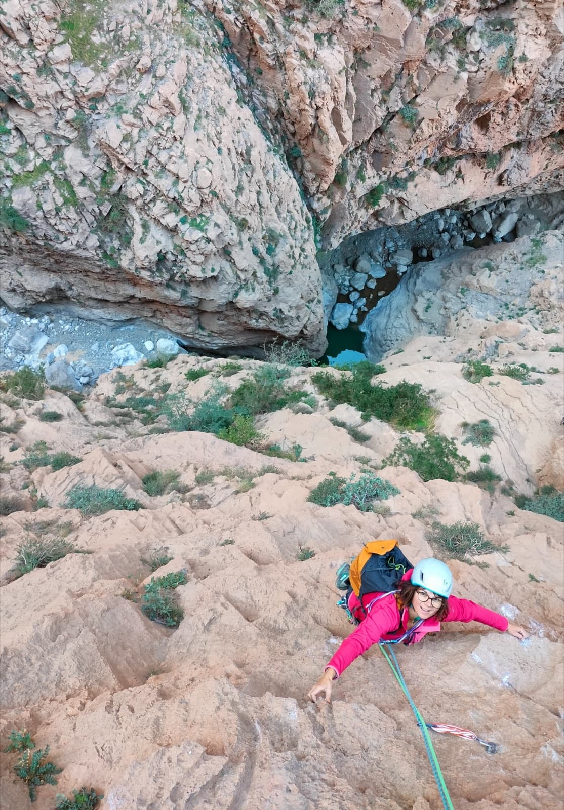 A climber on the red limestone of L'allumeur de rêves berbères, Timrazine, with the bed of the gorge far below.