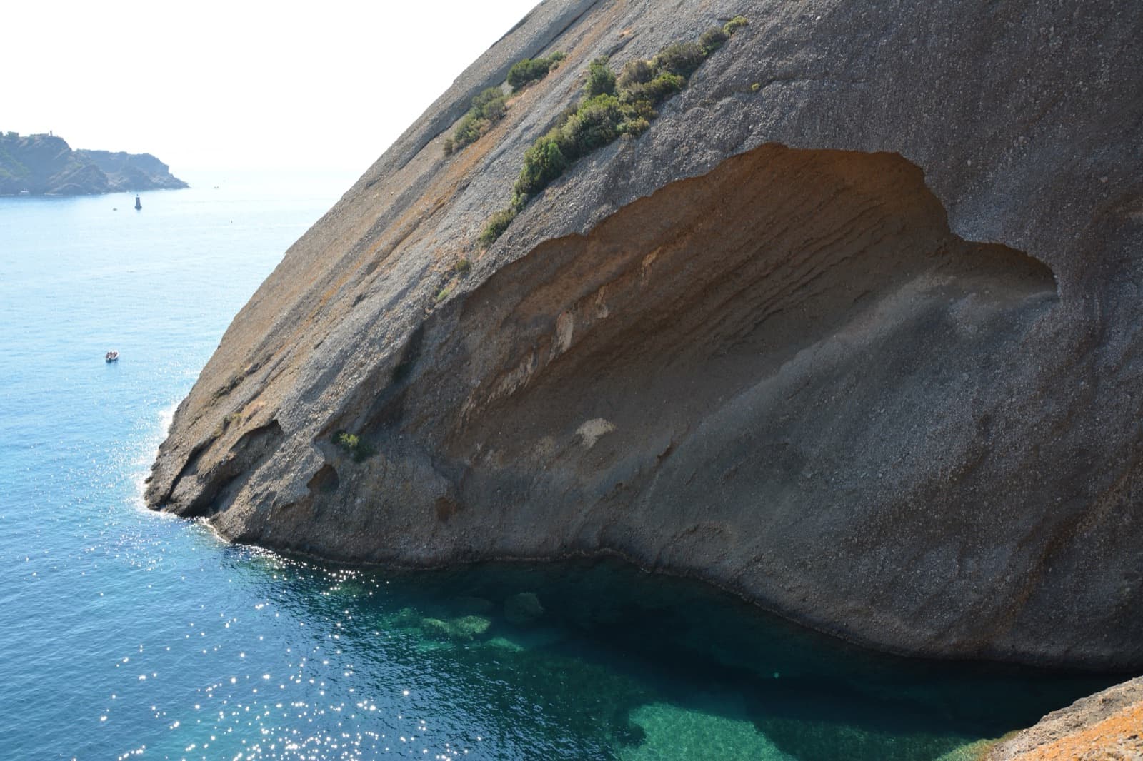 Close view of the puddingstone slab of the Bec de l'Aigle above the turquoise water of the Anse du Sec, from the terraces of the Parc du Mugel.