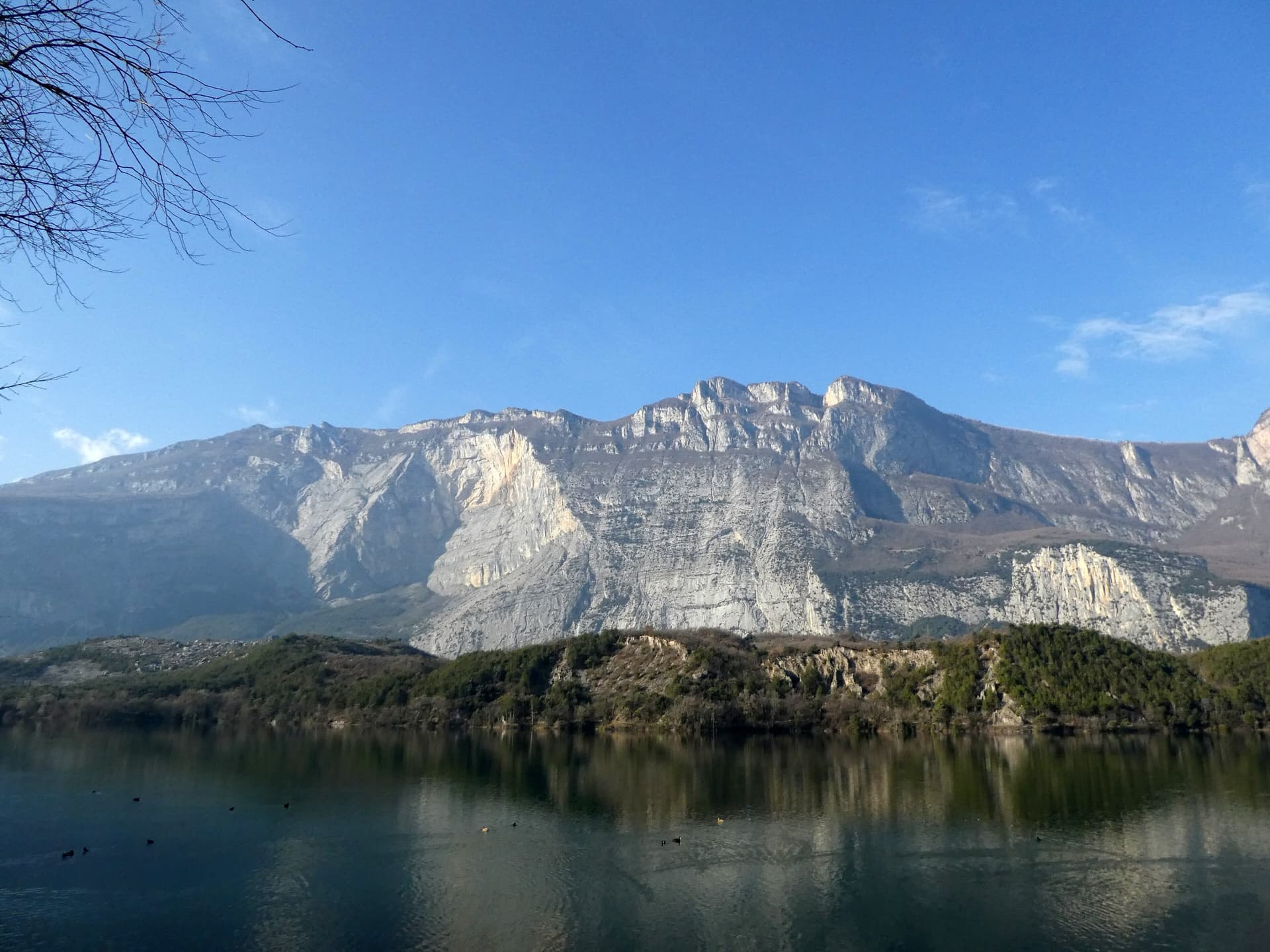 The east face of Monte Brento rising above Lago di Cavedine and the Marocche boulder field. The Placche Zebrate are the pale slab apron at the foot of the wall; the route's line is not marked.