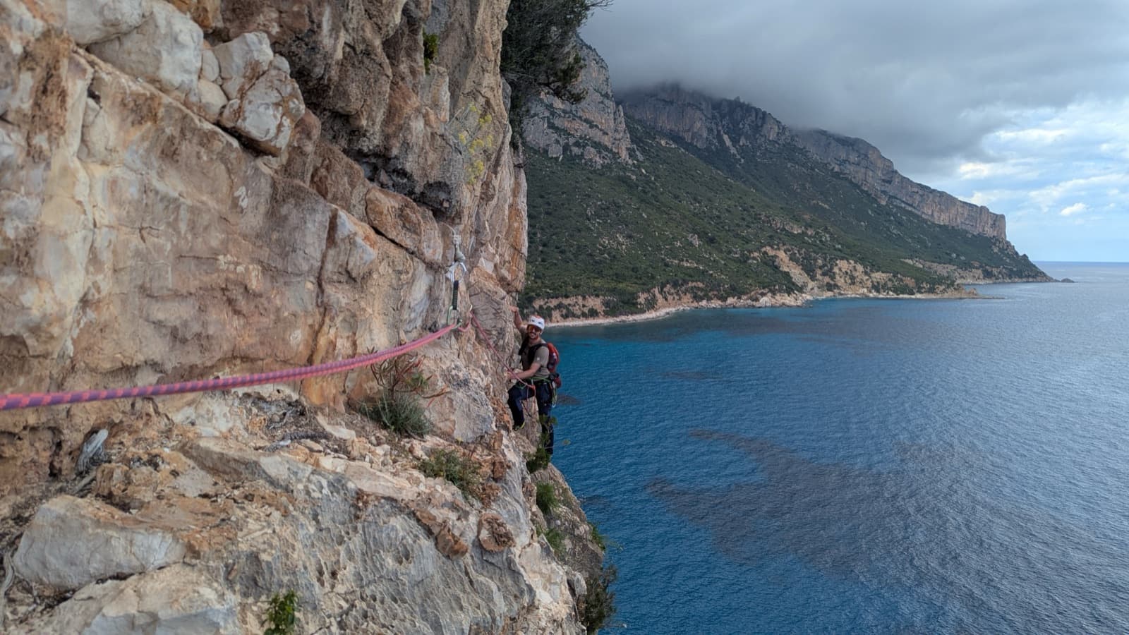 A climber on pitch 4 of Marinaio di Foresta, traversing above the sea with the Baunei coast behind.