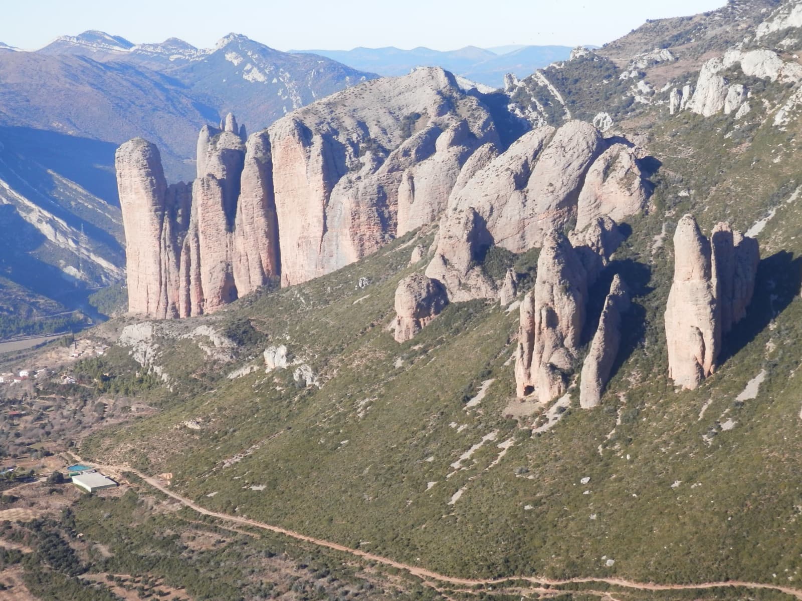 The Mallos de Riglos seen from the Os Fils massif to the east: the main wall on the left and the smaller eastern mallos scattered across the slope in the foreground.