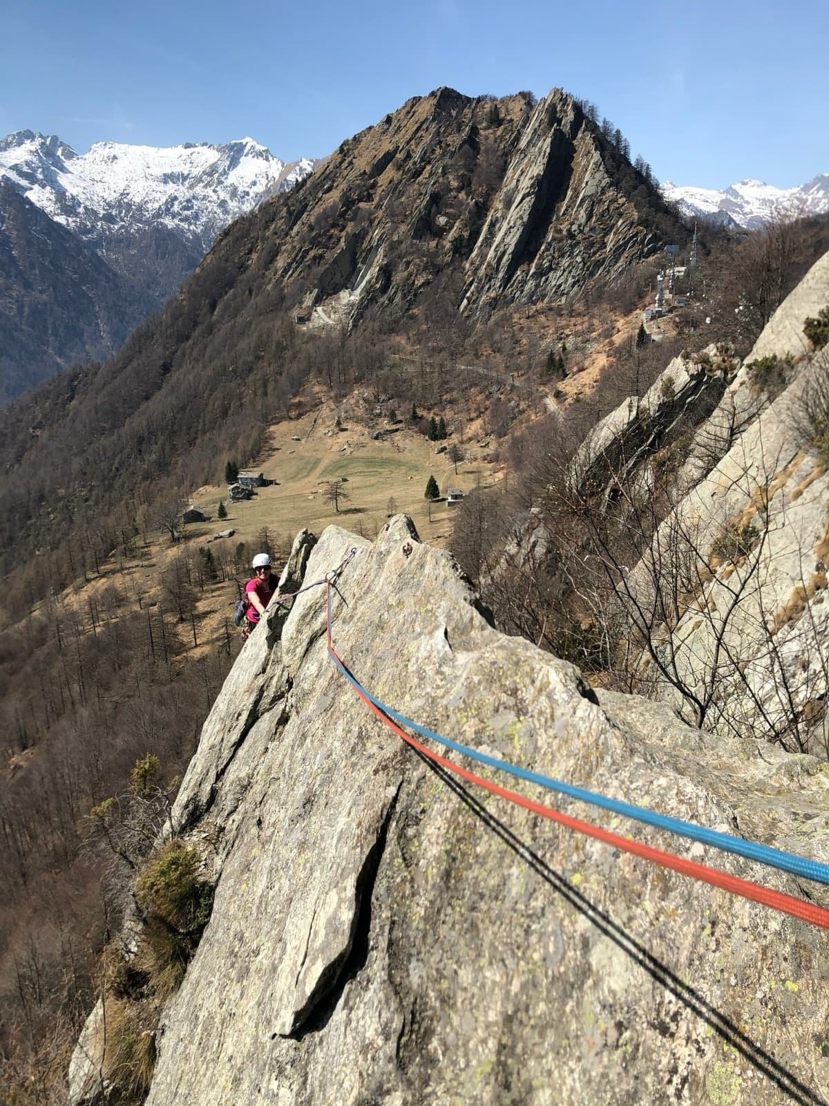 A climber following the gneiss arete of Spigolo Verde on the Serra di Biel, with alpine pastures and snowy peaks behind.