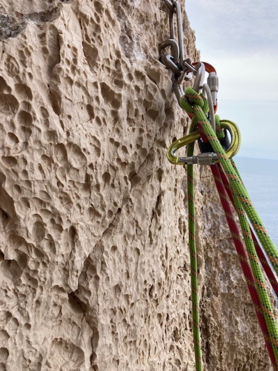 A chained belay on the pocketed limestone of Powaqqatsi, Capo Caccia