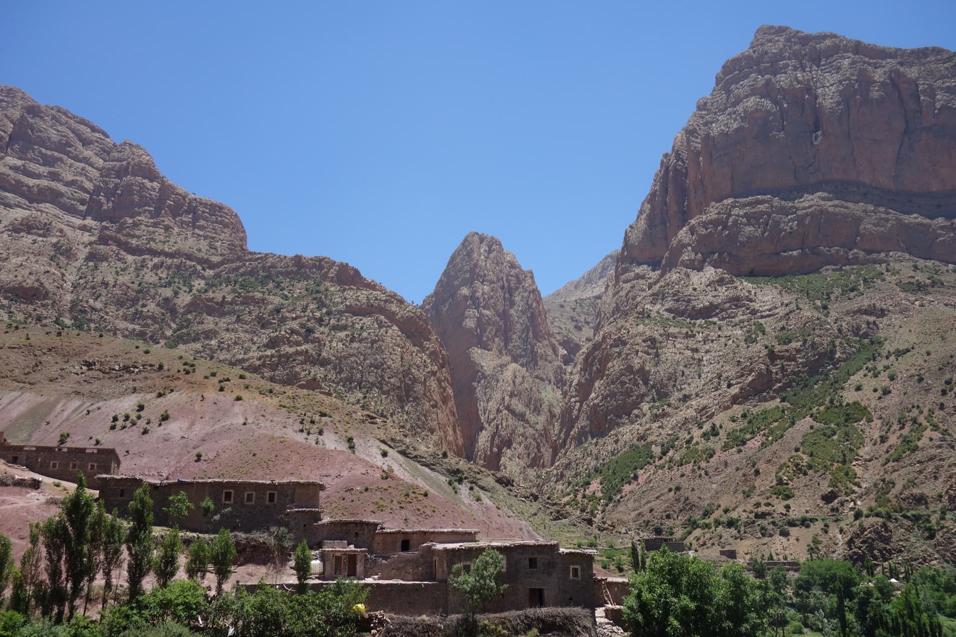 Taghia village beneath the pointed tower of the Taoujdad (centre), with the Oujdad massif at the right; the west face is the tower's right-hand flank, turned towards the Oujdad.